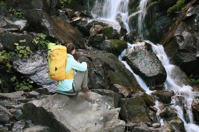 Photo of Tourist with yellow backpack enjoying mountain waterfall