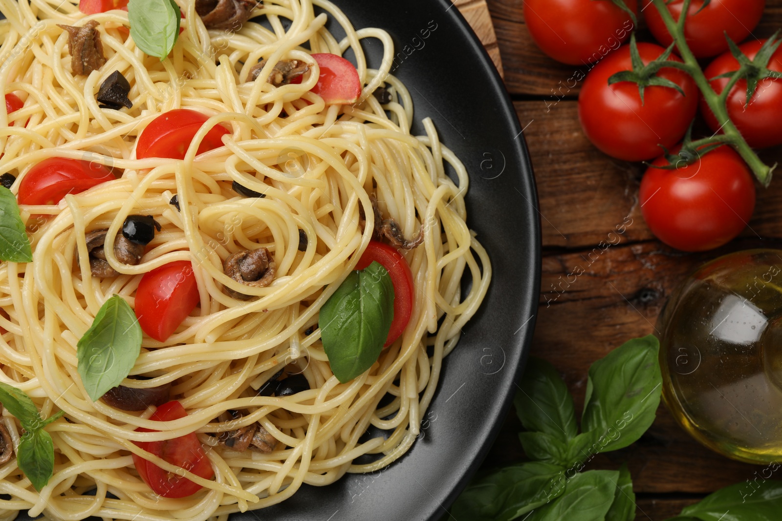 Photo of Delicious pasta with anchovies, tomatoes and basil on wooden table, flat lay