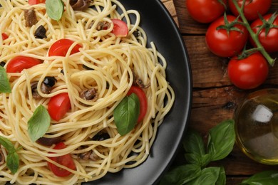 Delicious pasta with anchovies, tomatoes and basil on wooden table, flat lay