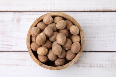Photo of Whole nutmegs in bowl on light wooden table, top view