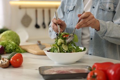 Photo of Woman making salad at white marble table in kitchen, closeup