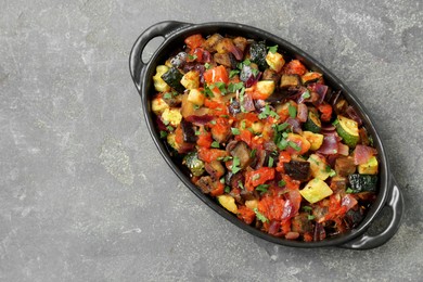 Photo of Dish with tasty ratatouille on grey textured table, top view. Space for text