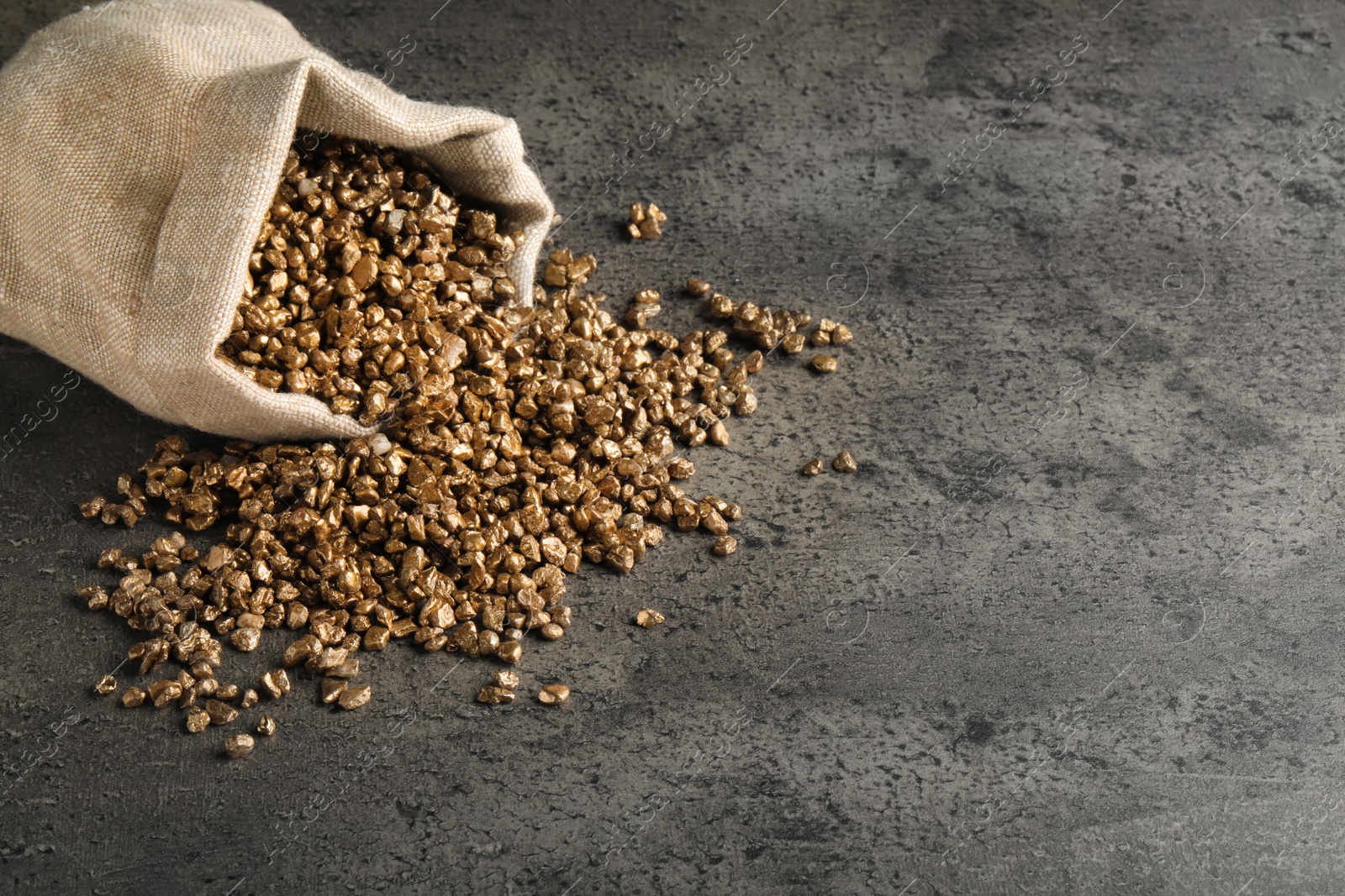 Photo of Overturned sack of gold nuggets on grey table, space for text