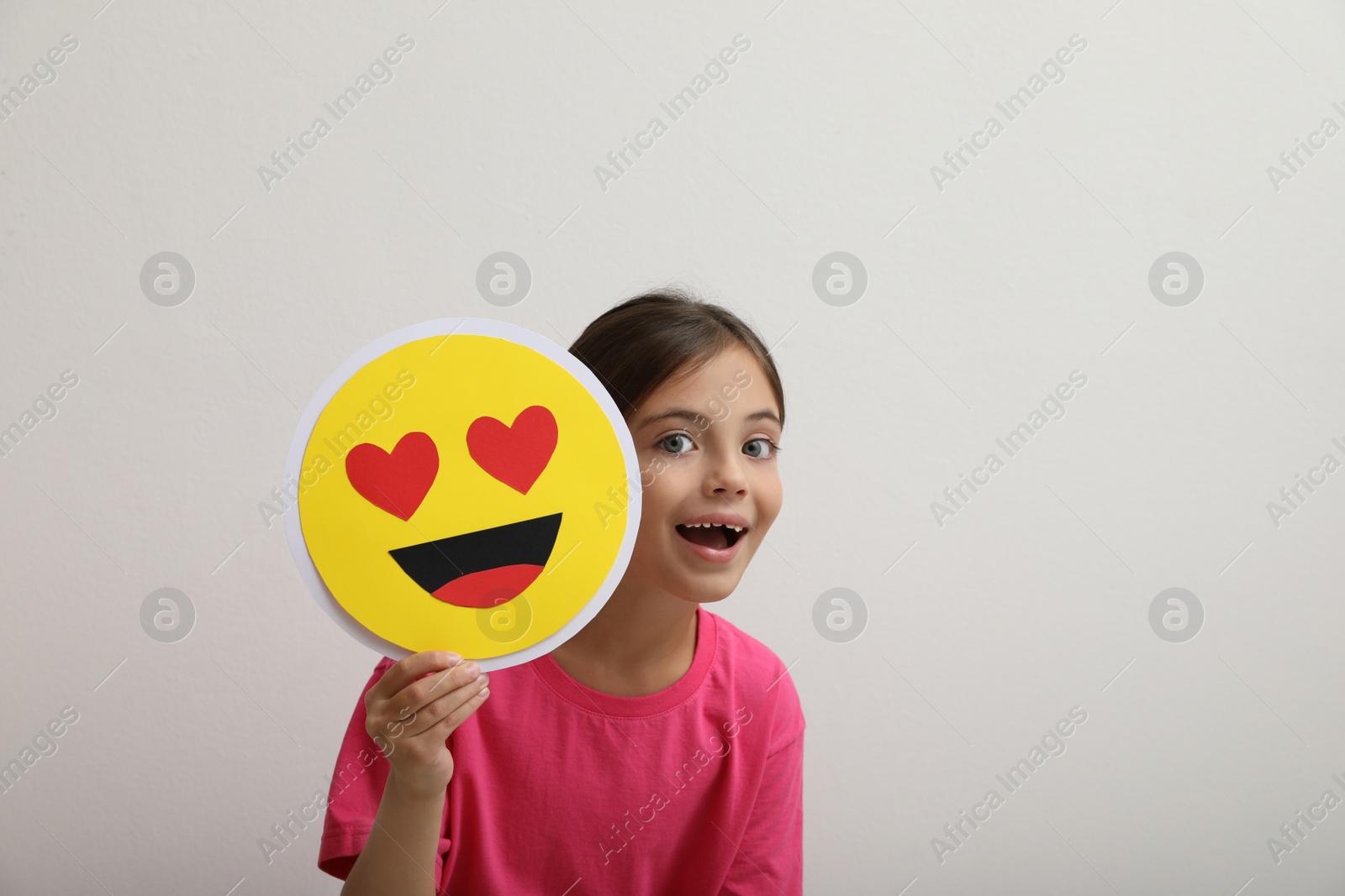 Photo of Little girl holding face with heart eyes emoji on white background