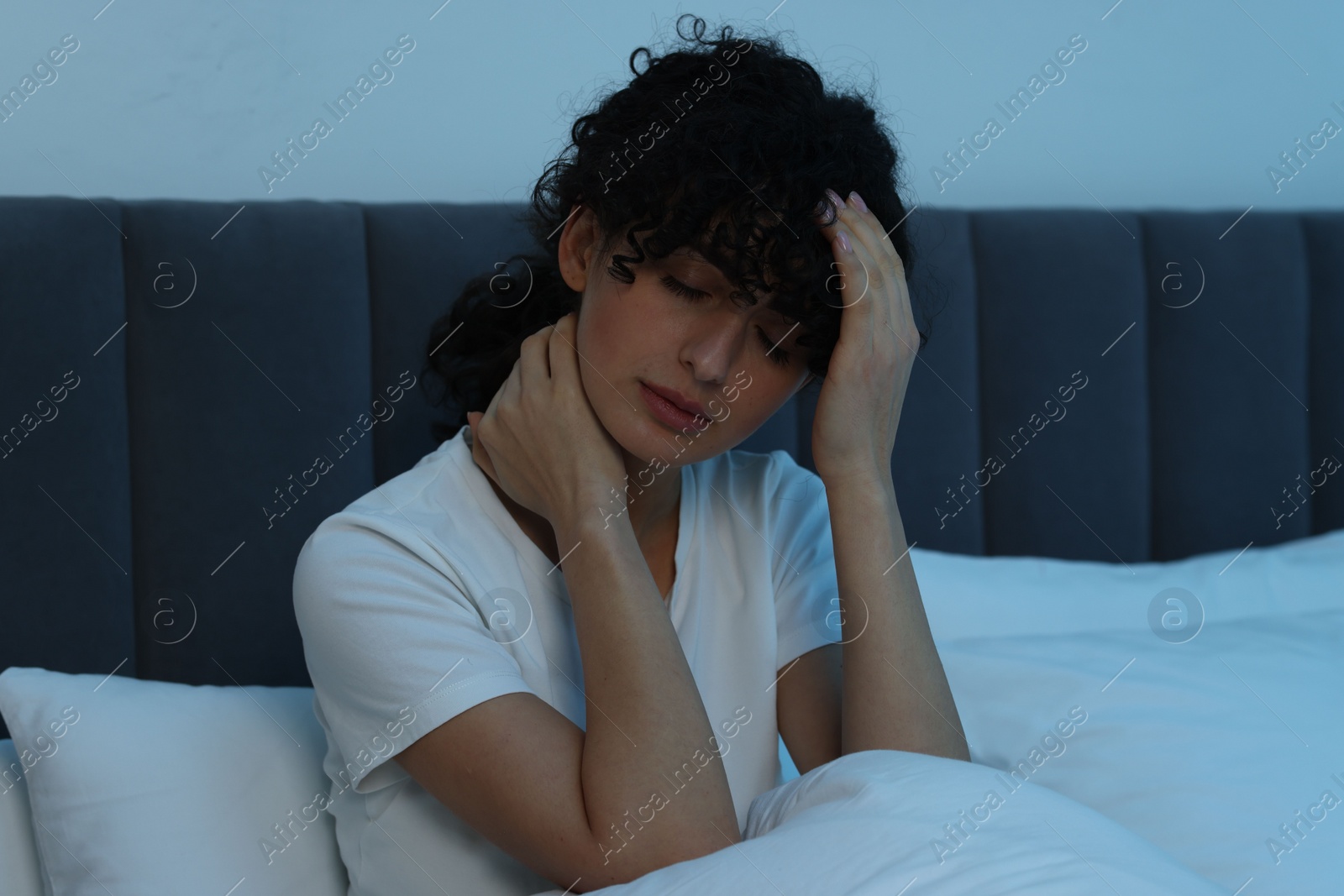 Photo of Young woman suffering from headache in bed at night