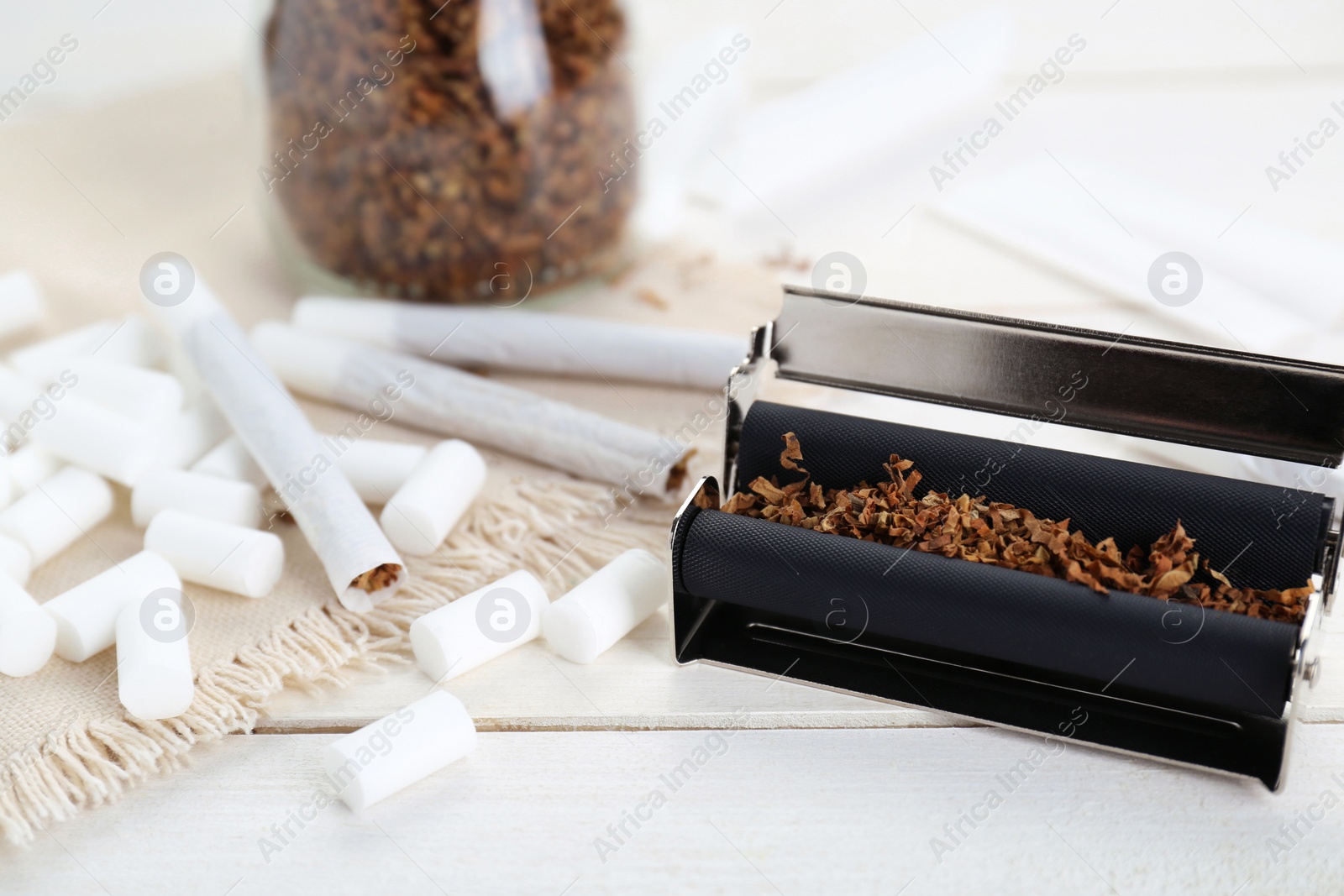 Photo of Hand rolled cigarettes, filters and tobacco on white wooden table, closeup