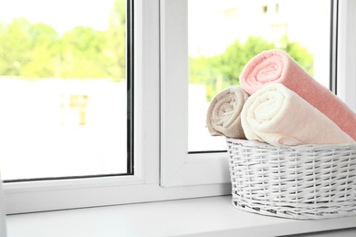 Photo of Basket with clean soft towels on window sill. Space for text