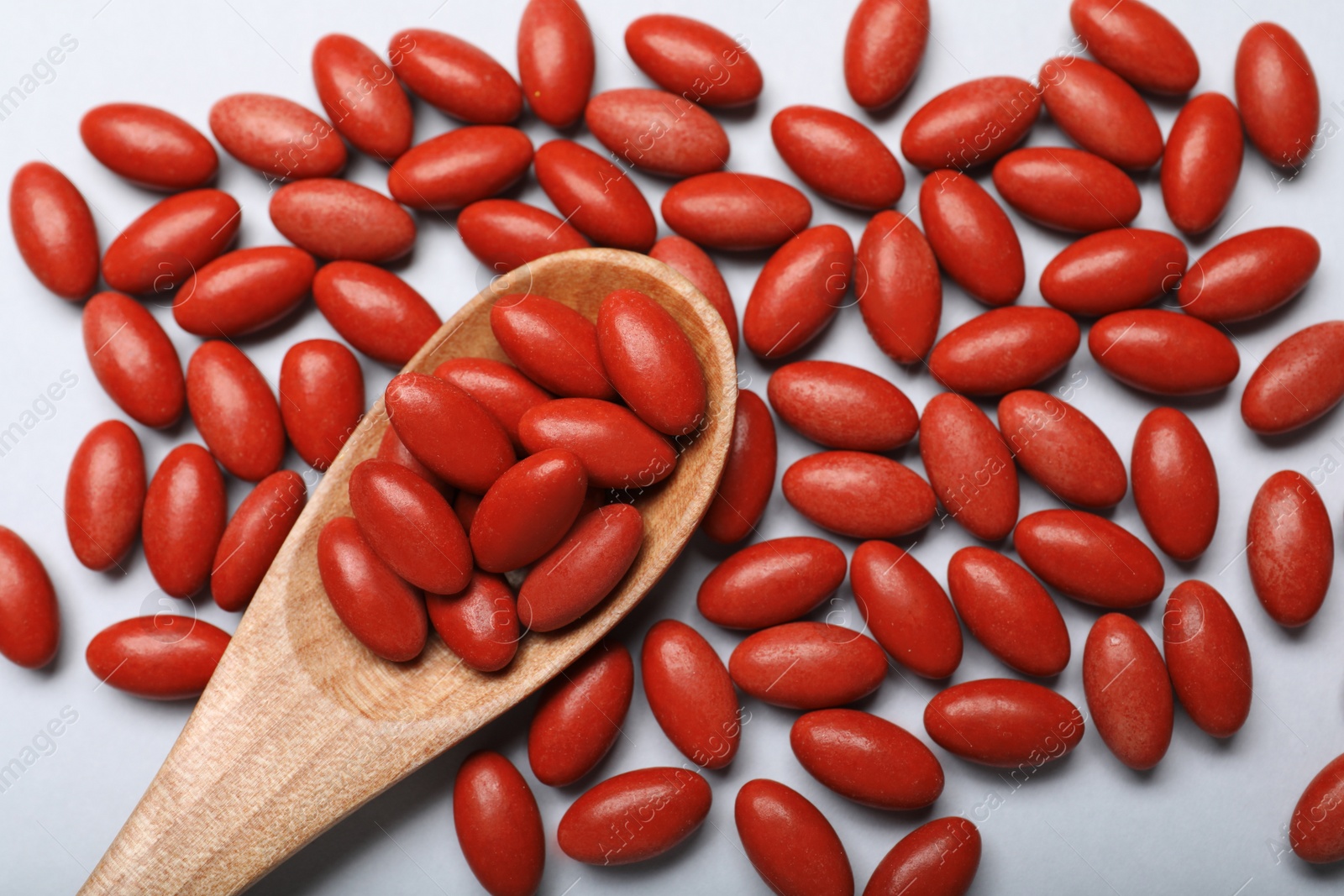 Photo of Wooden spoon and red pills on white background, flat lay. Anemia treatment