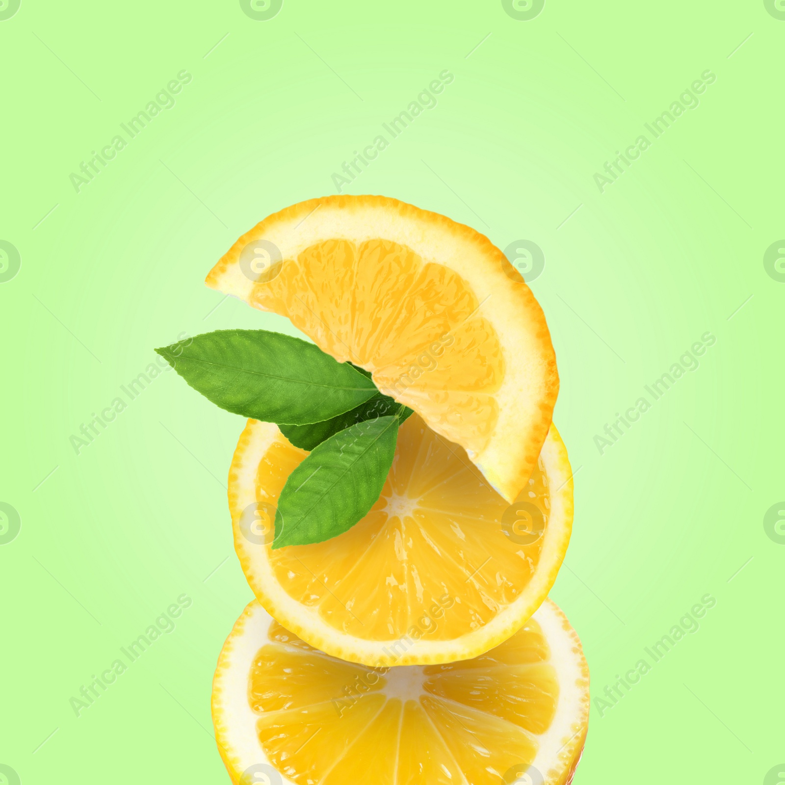 Image of Stack of cut fresh lemons with leaves on light green background