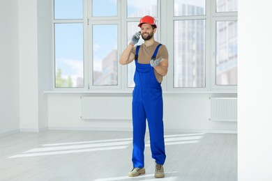 Professional repairman in uniform talking on phone indoors, space for text