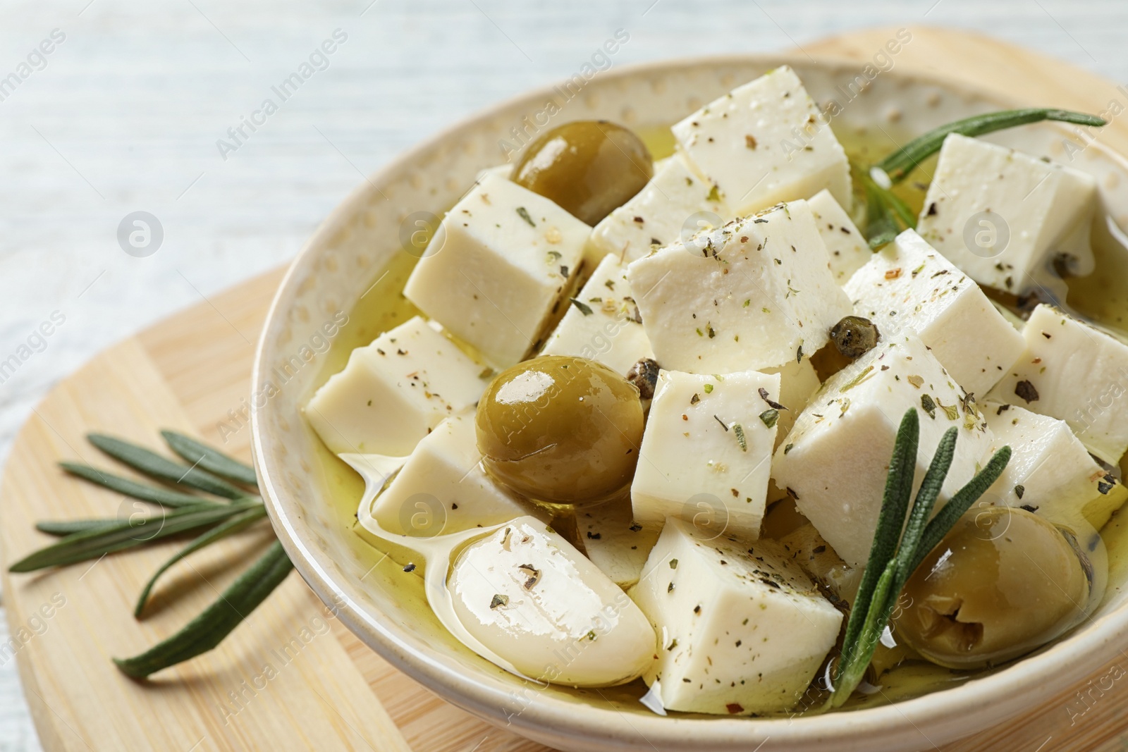 Photo of Pickled feta cheese in bowl on wooden board, closeup