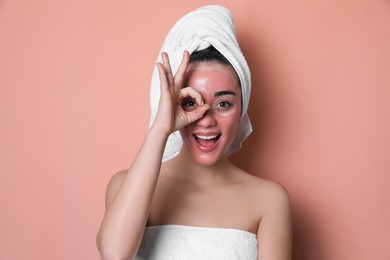 Woman with pomegranate face mask showing Ok on pale coral background