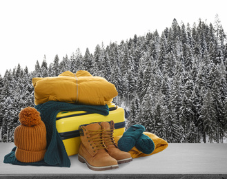 Image of Suitcase with warm clothes on stone surface against beautiful winter landscape. Space for text