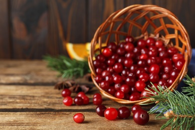 Photo of Overturned basket with fresh ripe cranberries on wooden table. Space for text