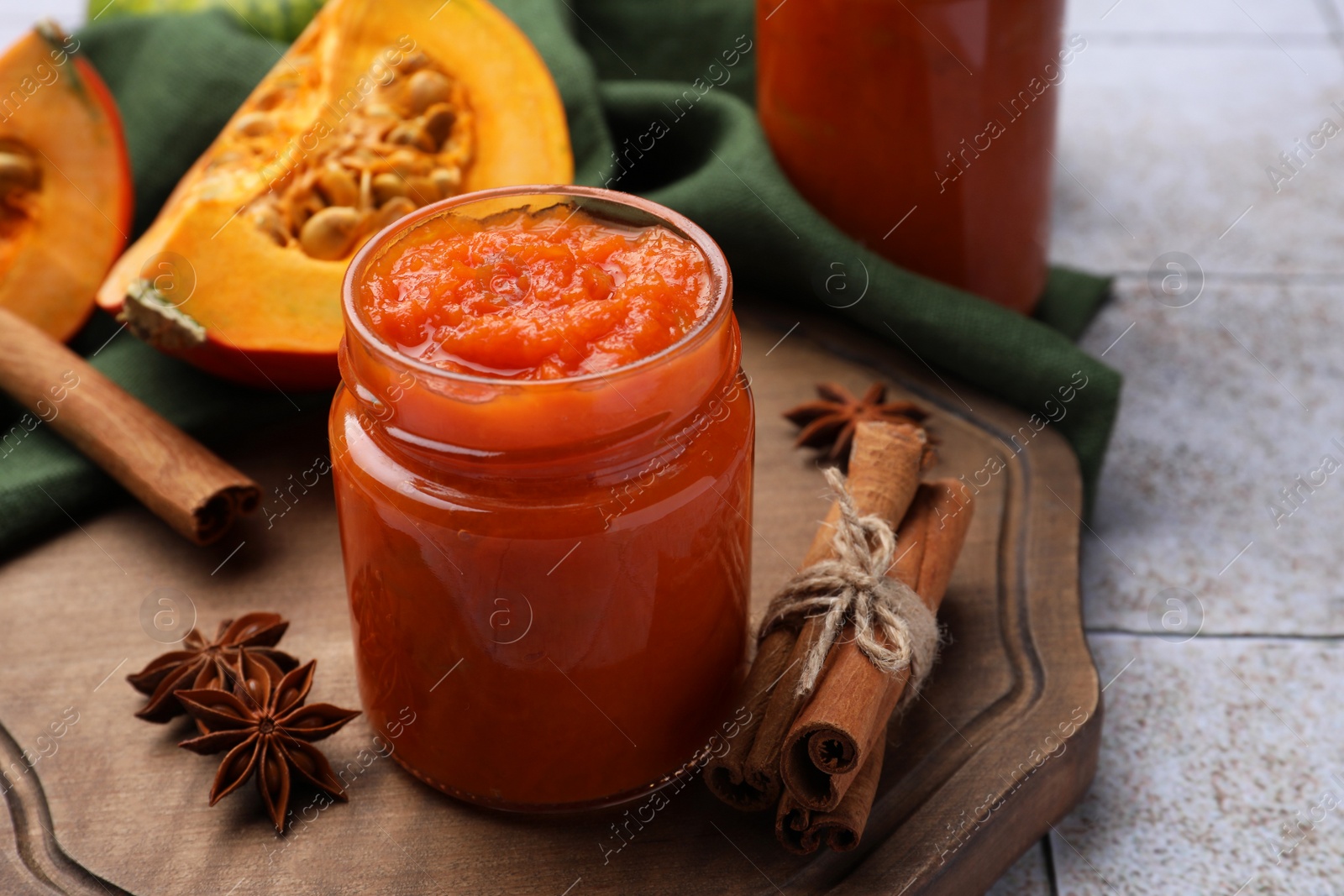 Photo of Jar of delicious pumpkin jam and ingredients on tiled surface, closeup