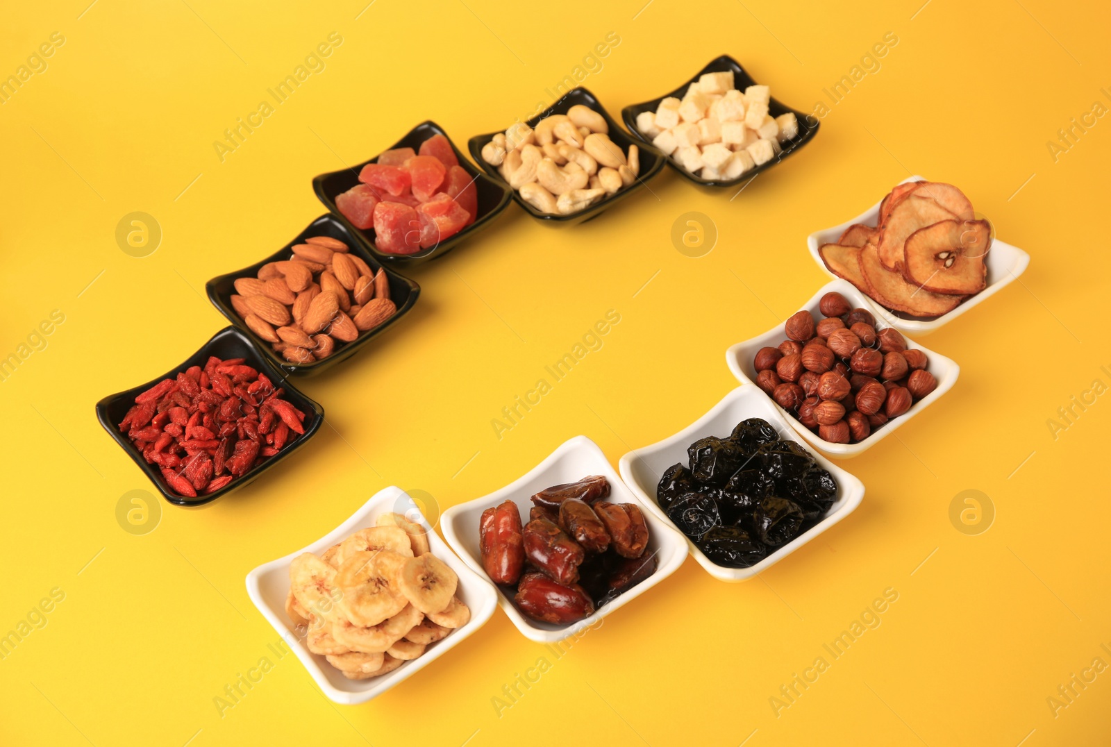 Photo of Bowls with dried fruits and nuts on yellow background