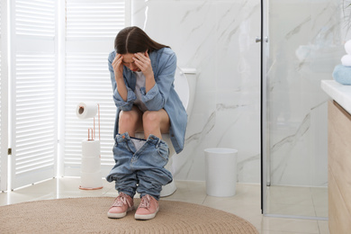 Photo of Woman suffering from hemorrhoid on toilet bowl in rest room