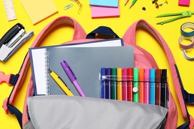 Photo of Flat lay composition with backpack and school stationery on yellow background