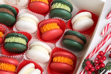 Different tasty Christmas macarons in box and festive decor on white table, above view