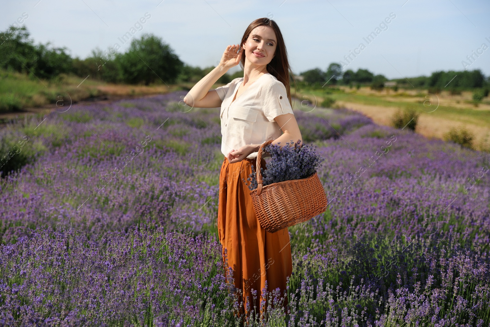 Photo of Young woman with wicker basket full of lavender flowers in field