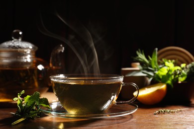 Photo of Cup of aromatic herbal tea, mint and rosemary on wooden table