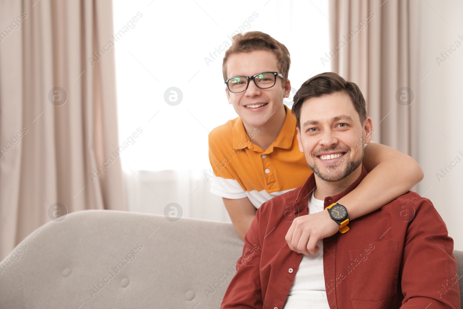 Photo of Happy teenager hugging his father at home. Space for text