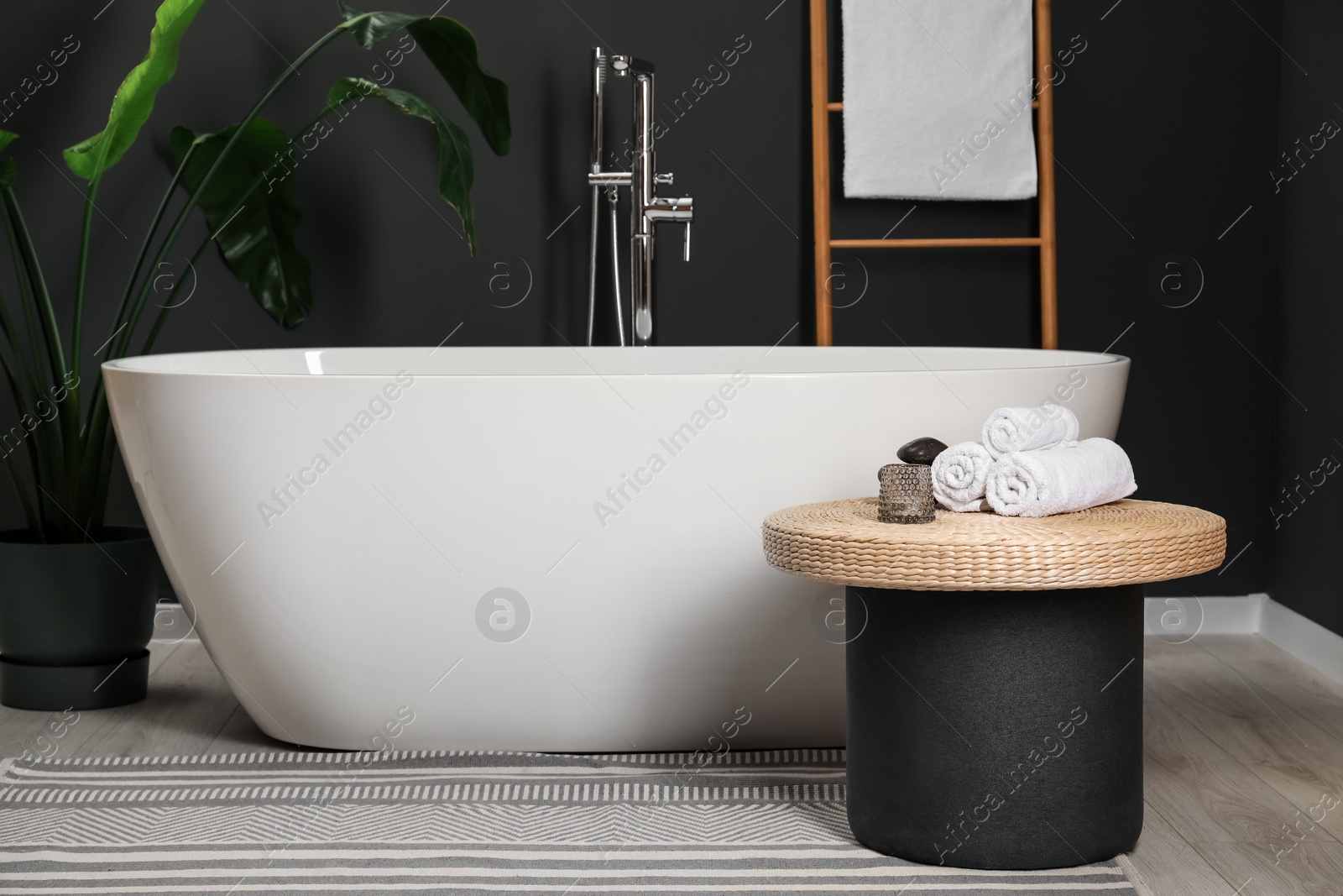 Photo of Spa day. Ceramic tub, houseplant and wicker table in bathroom