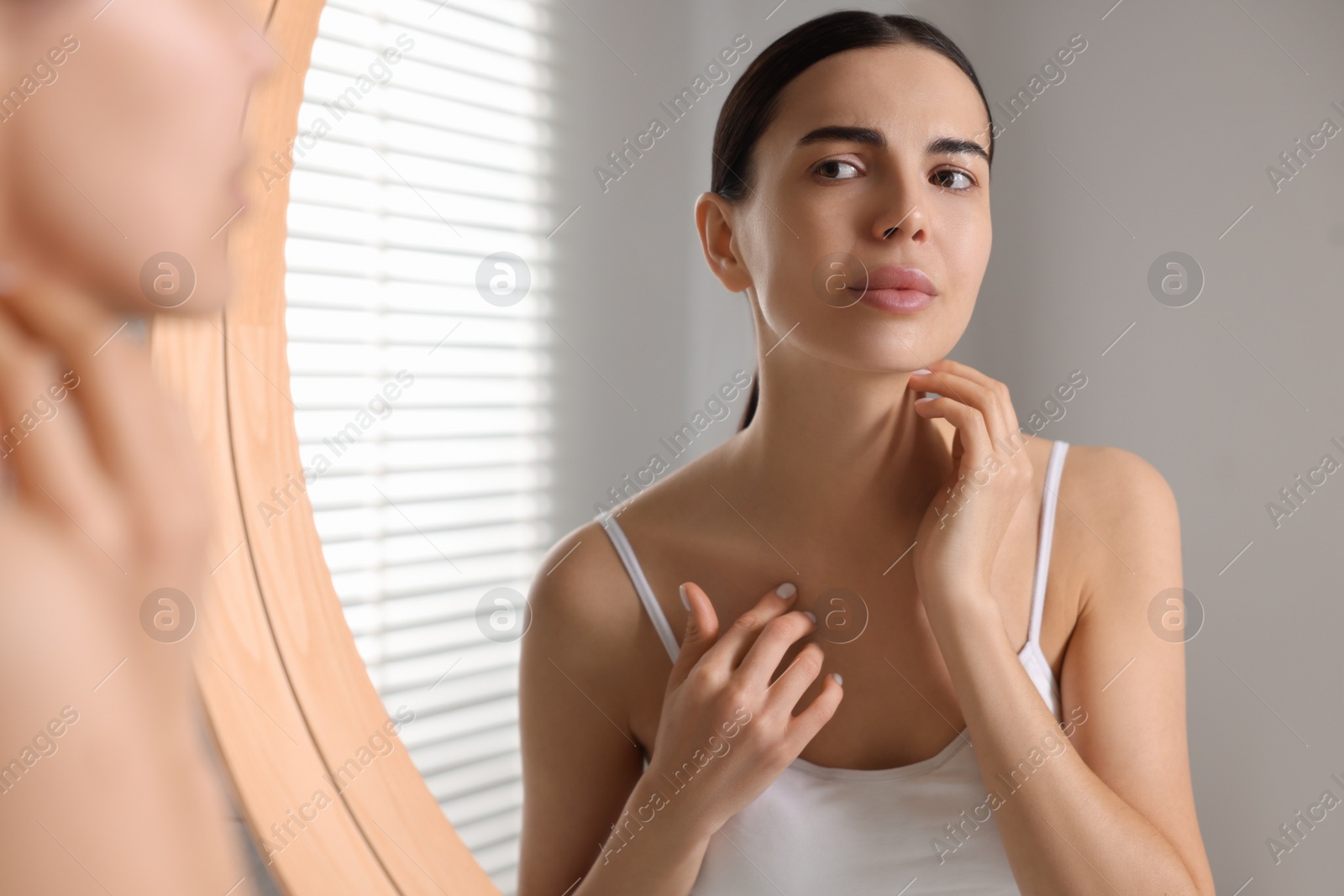 Photo of Woman with dry skin looking at mirror in bathroom