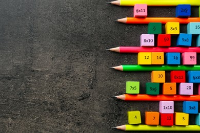 Photo of Many colorful cubes with numbers, multiplications and pencils on dark grey table, flat lay. Space for text