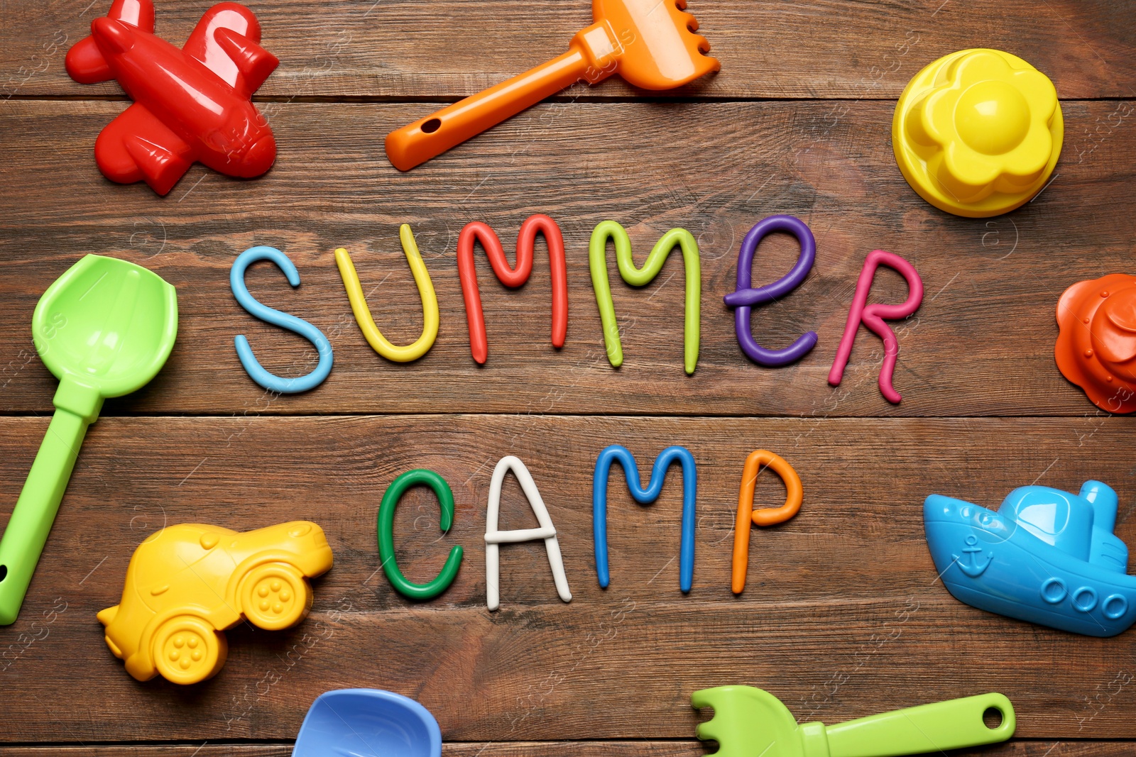 Photo of Text SUMMER CAMP made of modelling clay and different sand molds on wooden table, flat lay