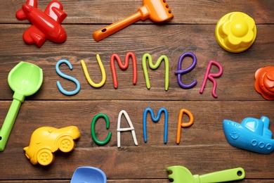 Text SUMMER CAMP made of modelling clay and different sand molds on wooden table, flat lay