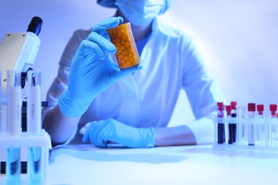 Photo of Scientist with pills at table in laboratory, closeup