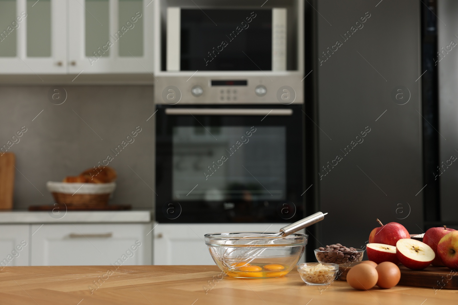 Photo of Cooking process. Metal whisk, bowl and products on wooden table in kitchen. Space for text