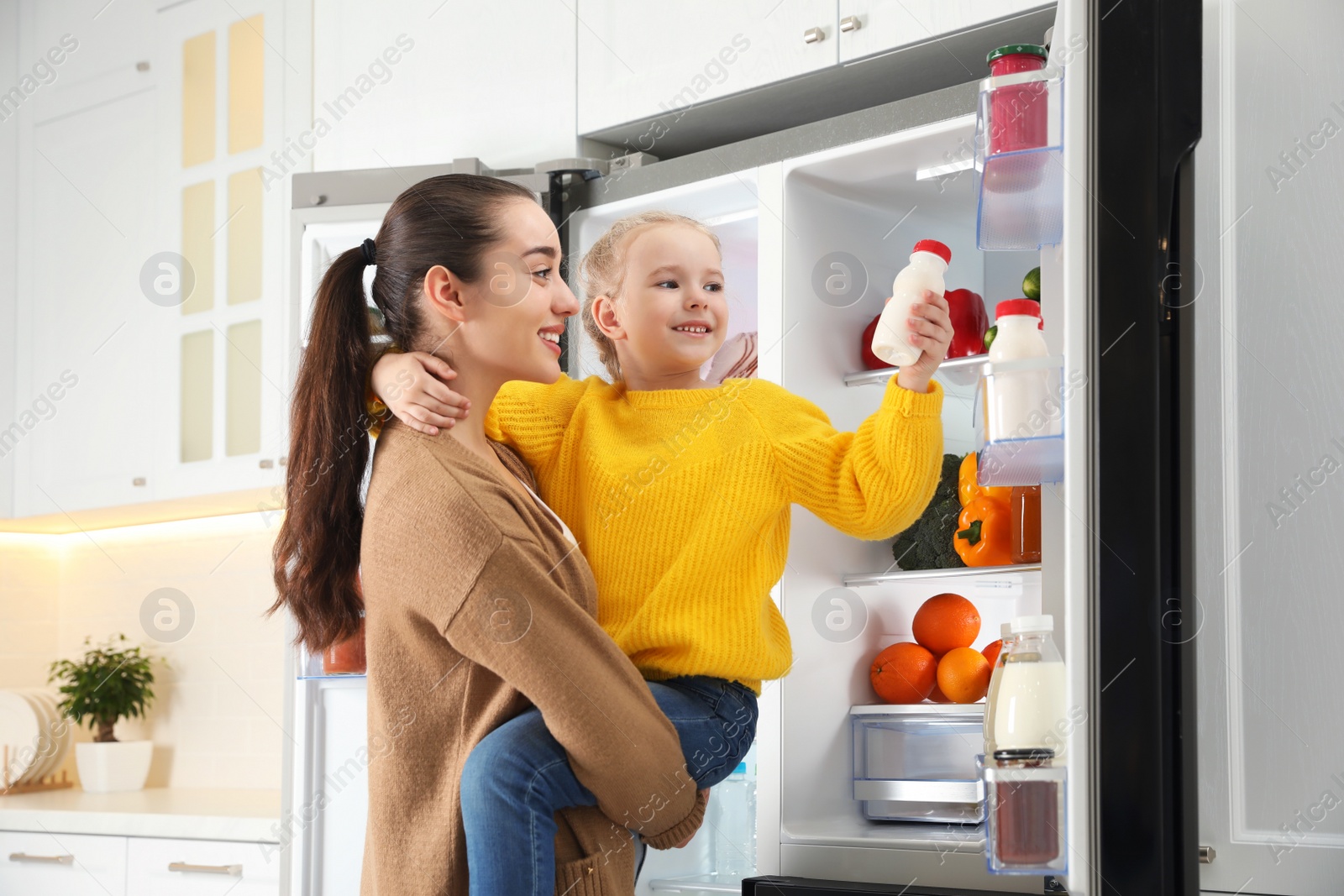 Photo of Young mother and daughter near open refrigerator in kitchen