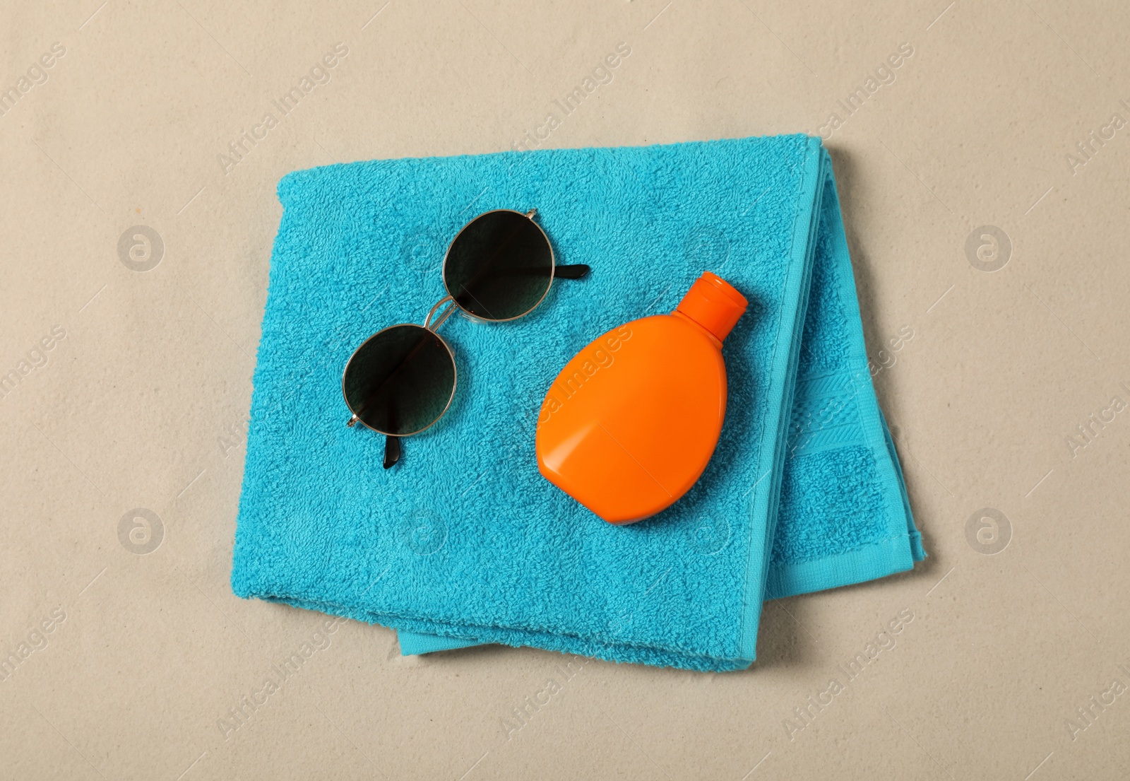 Photo of Beach towel, sunglasses and sunscreen on sand, top view