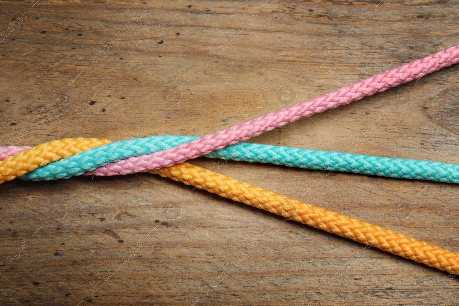 Photo of Twisted colorful ropes on wooden background, top view. Unity concept