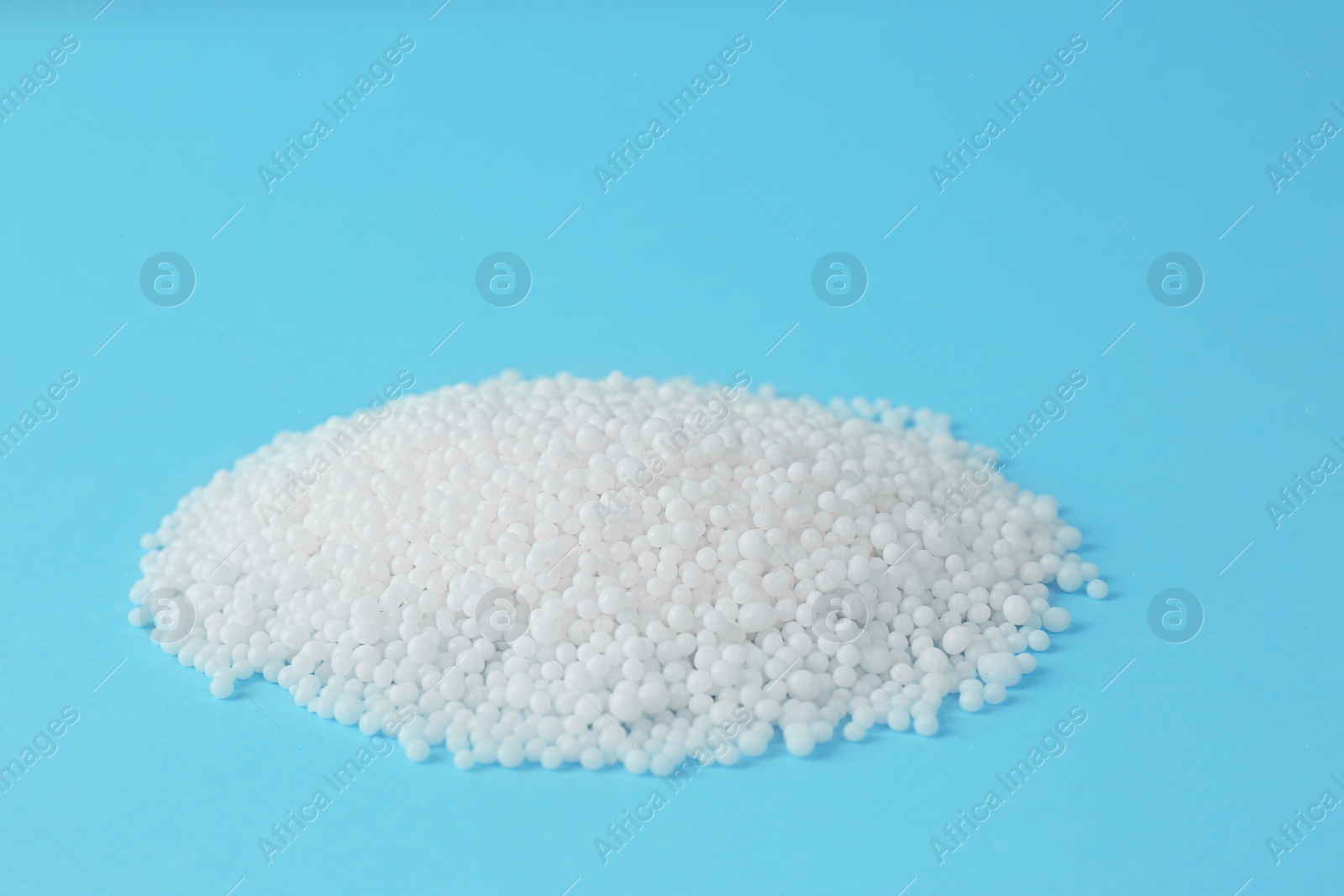 Photo of Pellets of ammonium nitrate on light blue background, space for text. Mineral fertilizer