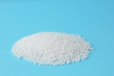 Pellets of ammonium nitrate on light blue background, space for text. Mineral fertilizer