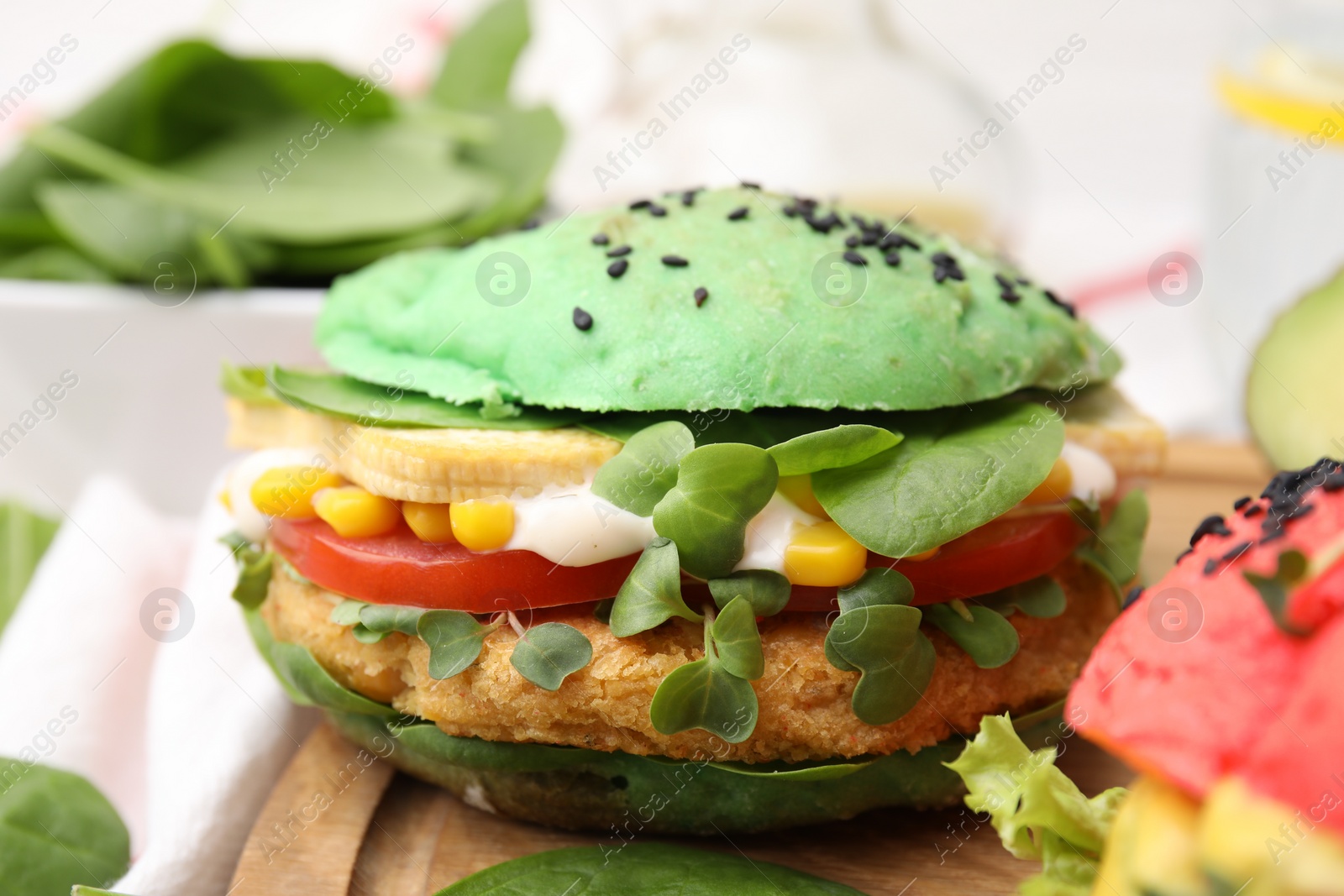 Photo of Tasty green vegan burger with vegetables, patty and microgreens on wooden board, closeup