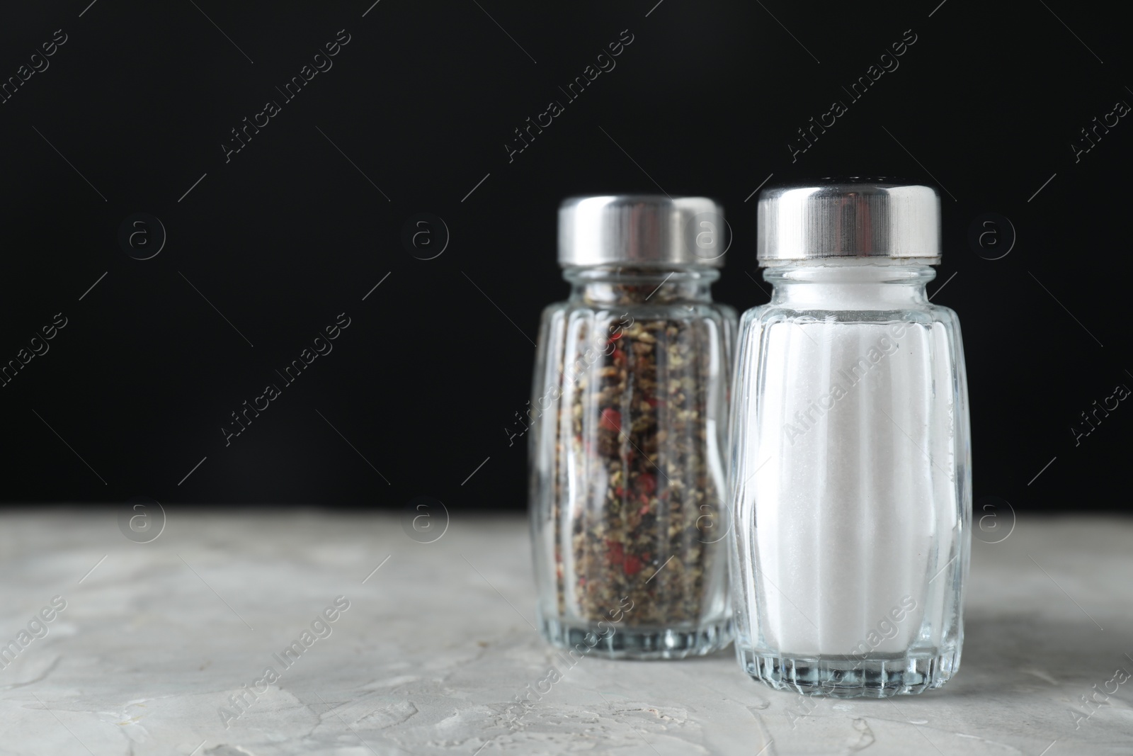 Photo of Salt and pepper shakers on light textured table against black background. Space for text
