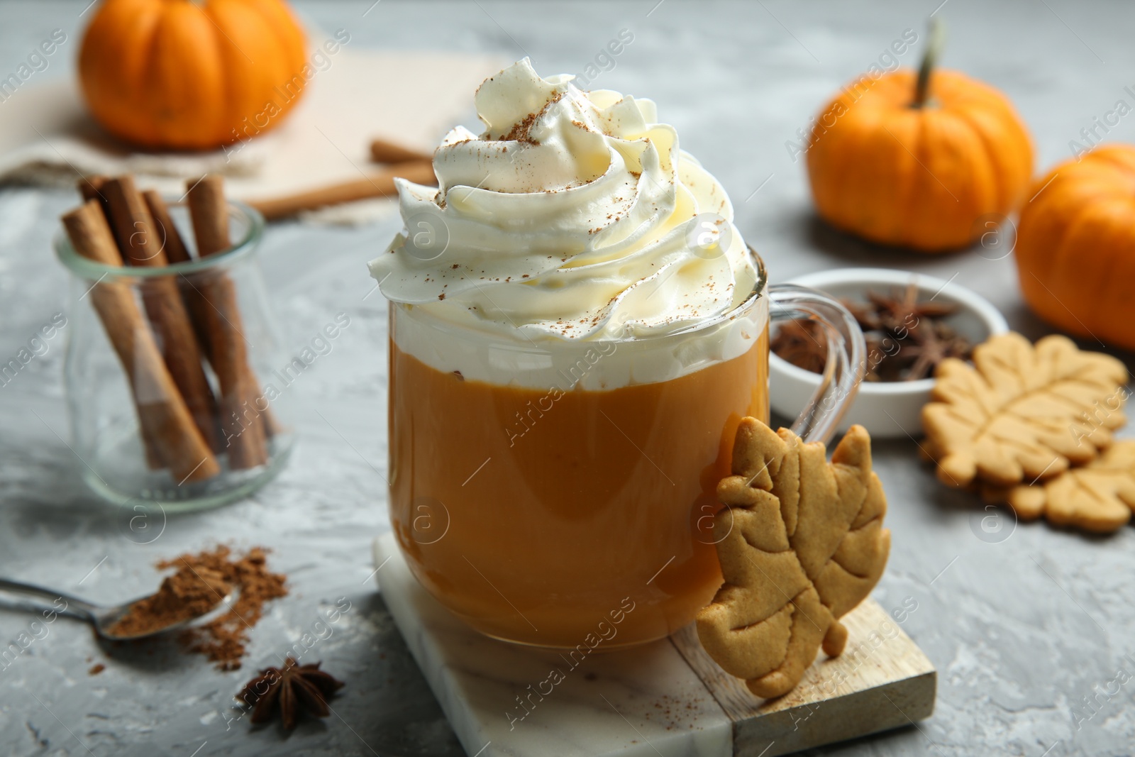 Photo of Cup of pumpkin spice latte with whipped cream, cookies and ingredients on light grey table, closeup