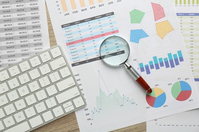 Accounting documents, magnifying glass and computer keyboard on wooden table, flat lay