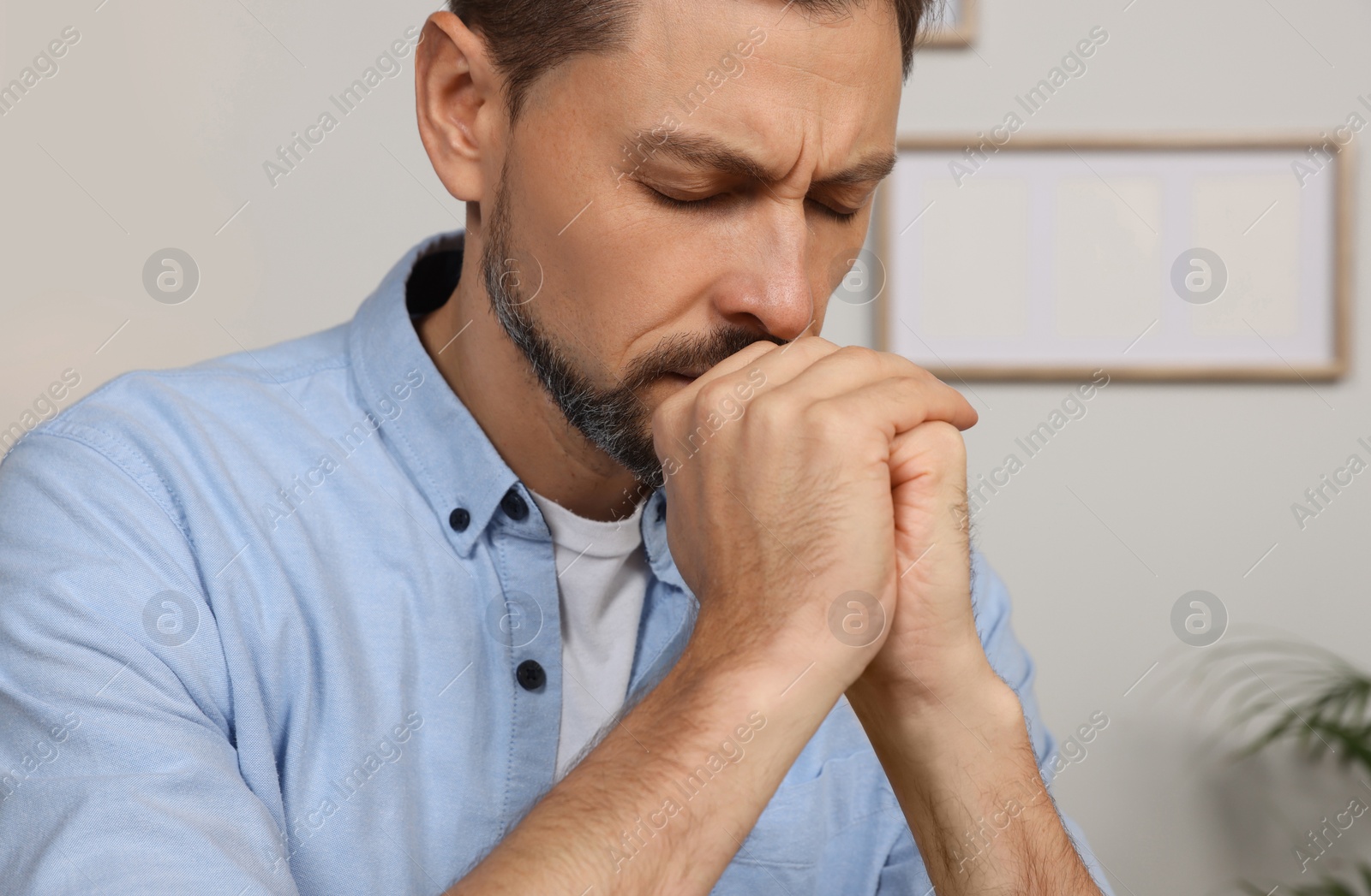 Photo of Man with clasped hands praying indoors, closeup