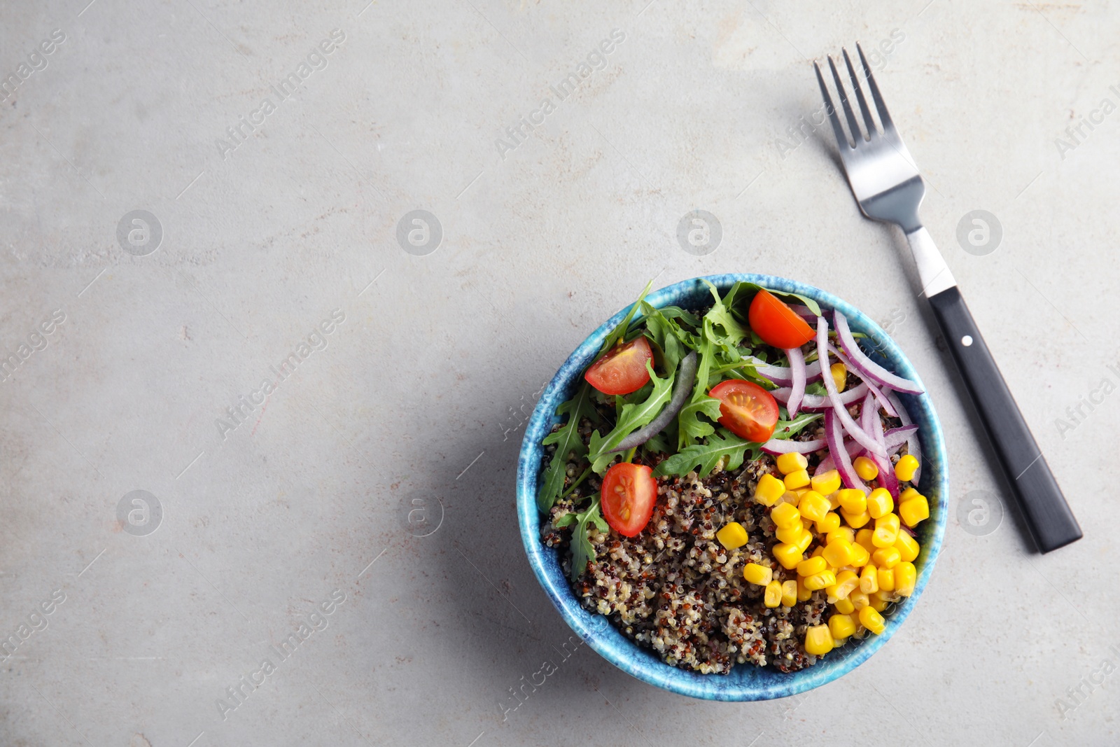 Photo of Healthy quinoa salad with vegetables in bowl and fork on color background, top view. Space for text