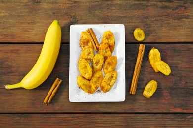 Photo of Tasty deep fried banana slices and cinnamon sticks on wooden table, flat lay