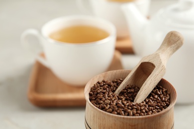 Bowl with buckwheat tea granules and wooden scoop on table, closeup. Space for text