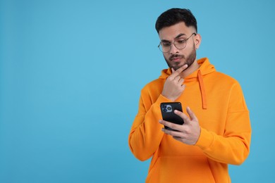 Photo of Handsome young man using smartphone on light blue background, space for text