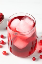 Photo of Tasty cranberry juice with ice cubes in glass and fresh berries on white wooden table, closeup