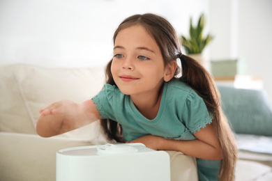 Photo of Little girl near modern air humidifier at home