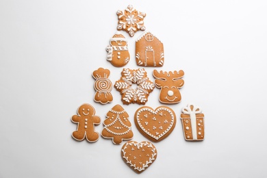 Photo of Christmas tree shape made of delicious decorated gingerbread cookies on white background, flat lay